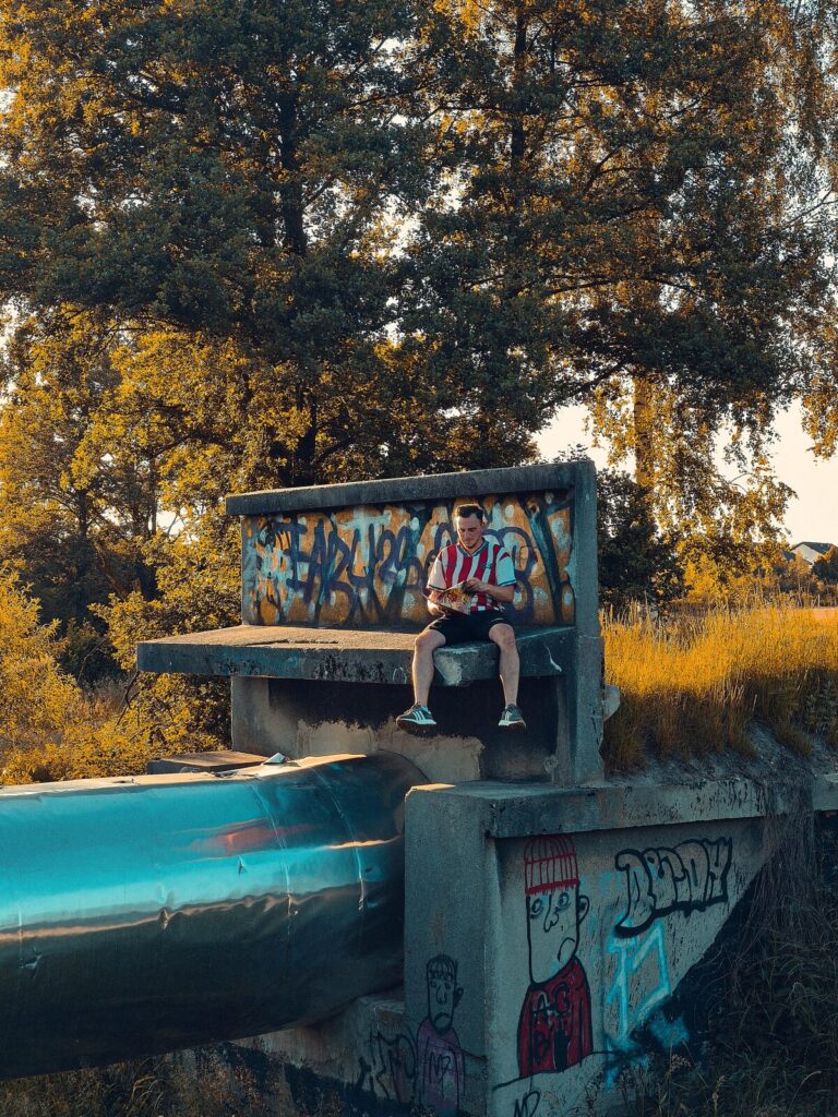 Fan in a red and white football shirt sitting on a concrete bench with graffiti